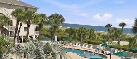 A resort with a pool area, palm trees, and a view of the ocean.