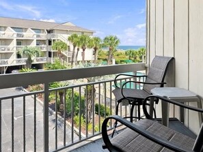 A balcony with two chairs and a table, overlooking a parking area and a building with balconies.