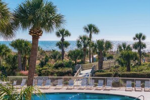 A pool area with lounge chairs, a sign indicating shallow water, and a view of the ocean. - Breakers Villa 221 - Walk to Beach, Shops and Dining (Hilton Head Island)
