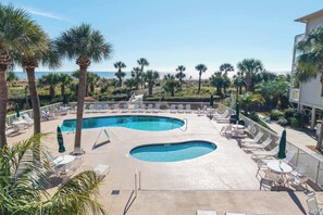 A pool area with two pools, lounge chairs, and umbrellas.