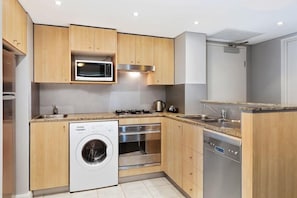 A compact kitchen with wooden cabinets, a built-in microwave, a washing machine, an oven, and a dishwasher. - Mantra Sydney Central (Sydney)