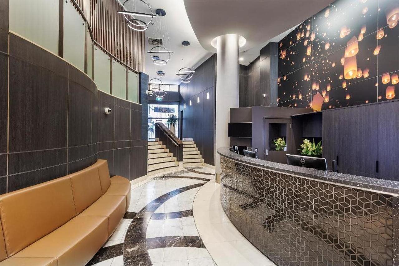 A modern lobby with a curved reception desk, a staircase, and a seating area.