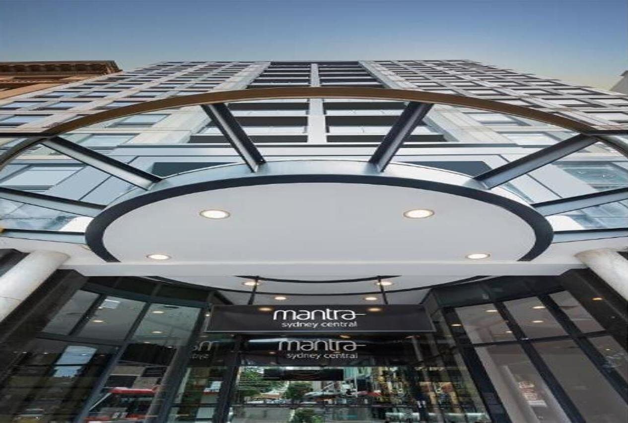 The exterior of a modern building with a curved glass facade and a sign reading "mantra sydney central".