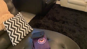 A living room with a black leather sofa, a white sofa, and a black furry rug. There is a radiator on the left and a window with blue curtains. - Two Families, up and Down Stairs, the 2nd Floor is the Vrbos Apartment (New Britain)