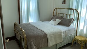 A single bed with a wooden frame, a white comforter, and two pillows. There is a small wicker chair and a light-colored rug on the floor. - Two Families, up and Down Stairs, the 2nd Floor is the Vrbos Apartment (New Britain)