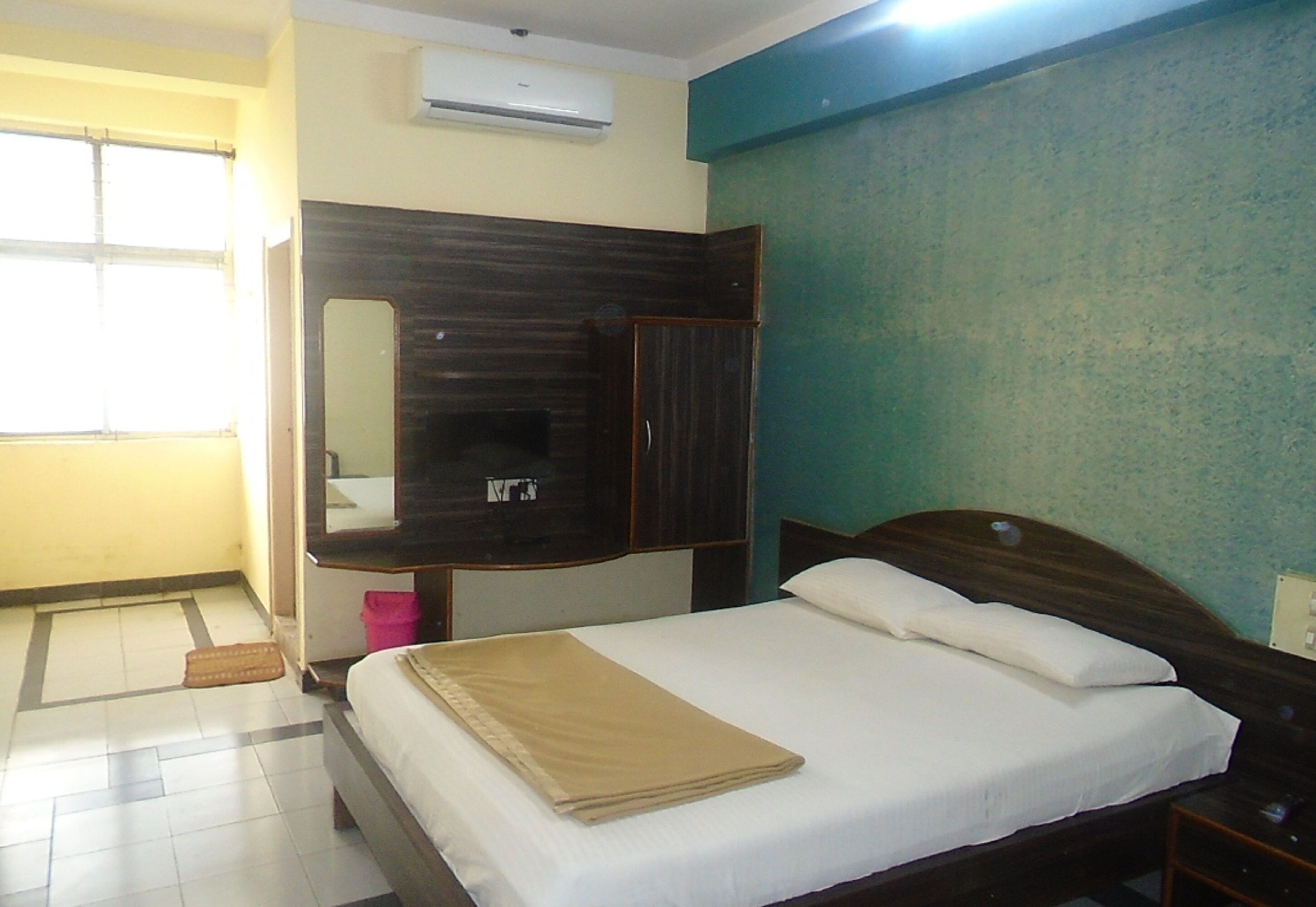 Una habitación de hotel con una cama, un armario, un espejo y un equipo de aire acondicionado.