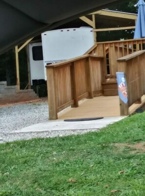 A covered outdoor area with a wooden deck, a white RV, and a blue umbrella.