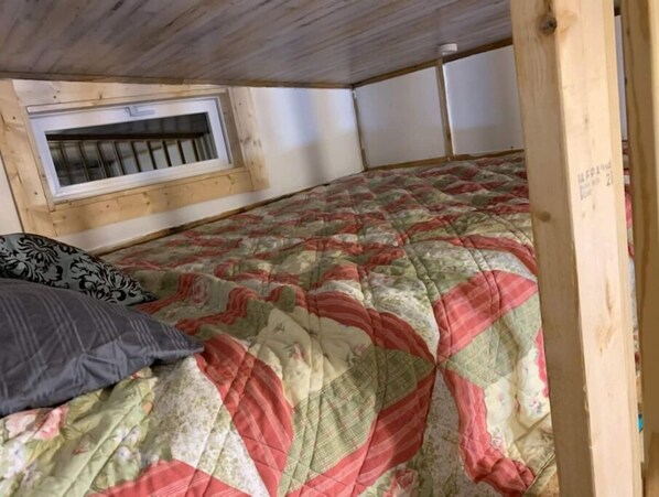 A bedroom with a window, a quilted bedspread, and a patterned pillow.