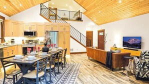 Une cuisine spacieuse avec des meubles en bois, un coin repas agrémenté d’un tapis à motifs, un escalier et un salon avec un canapé et une télévision.