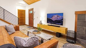 Un salon moderne avec un plafond en bois, un grand téléviseur à écran plat, un canapé en cuir, une table basse et une cheminée.
