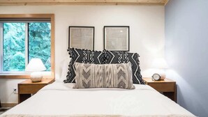 Una camera da letto con soffitto in legno, un letto grande con cuscini decorati, due comodini con lampade e opere d'arte incorniciate appese alla parete.
