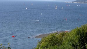 A coastal view with sailboats and windsurfers on the water, a beach with people, and a distant shoreline with buildings. - Peaceful Seattle Luxury Estate Romantic Seaview Guesthouse (Seattle)