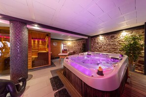 A spa area with a large hot tub, wooden walls, and a stone wall.