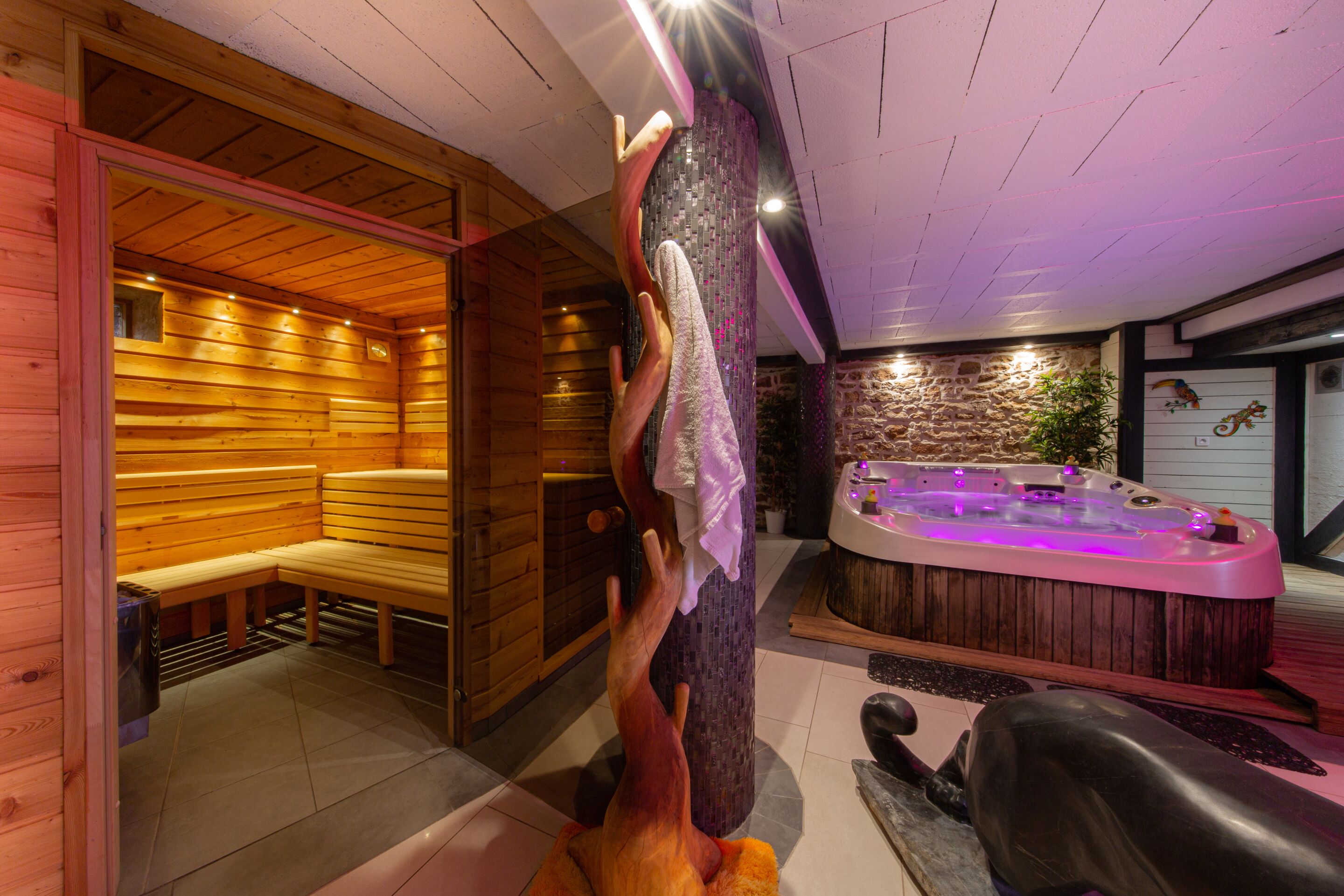 A sauna room with wooden benches and a hot tub with purple lighting.