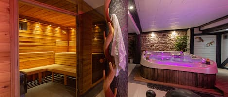 A sauna room with wooden benches and a hot tub with purple lighting.