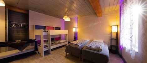 A room with bunk beds, a sofa, a hanging light fixture, and a wall-mounted lamp.