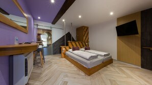 Een slaapkamer met een visgraatvloer, een bed met houten hoofdeinde, een houten bureau, een spiegel en een televisie aan de muur.