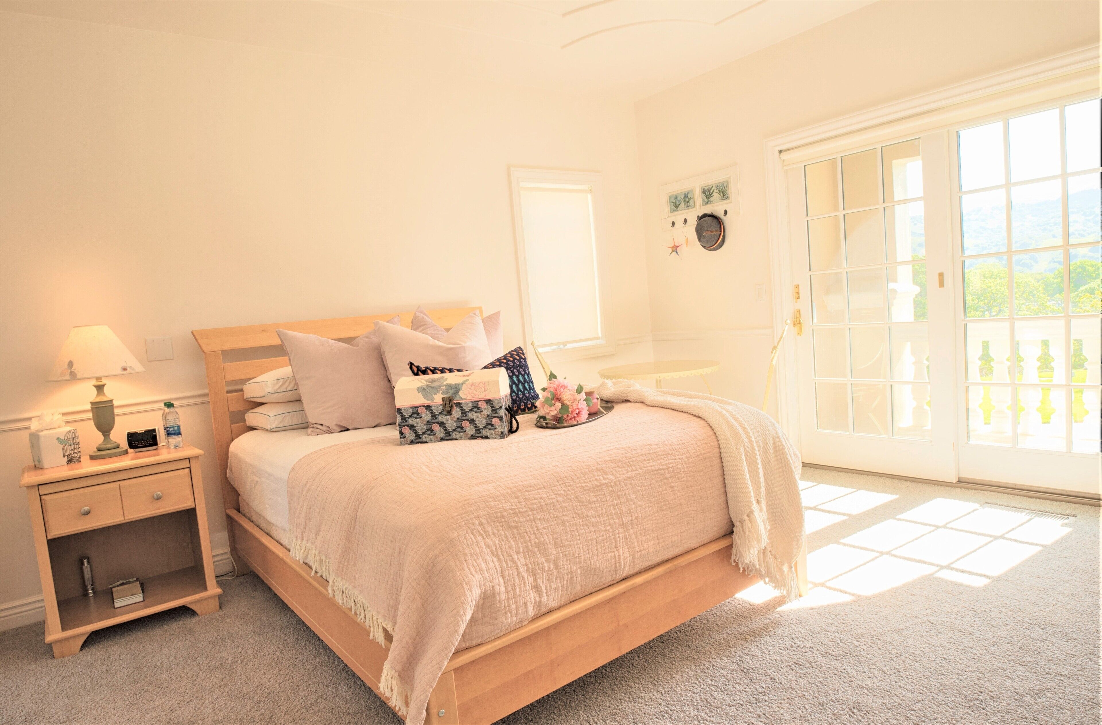 A bedroom with a bed, bedside table, lamp, and a view of the outdoors through a large window.