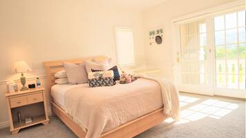 A bedroom with a bed, bedside table, lamp, and a view of the outdoors through a large window.