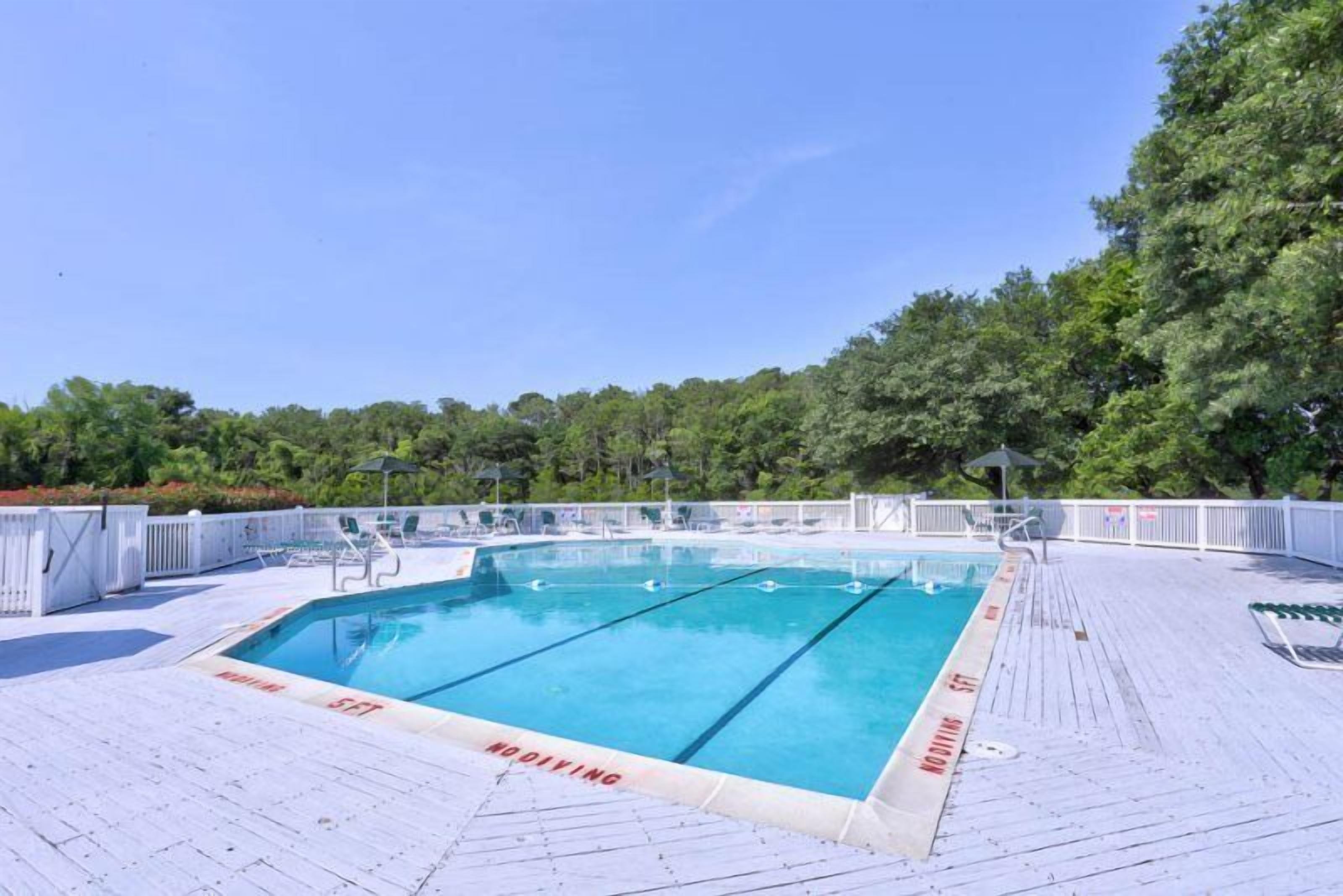 A rectangular swimming pool with clear blue water, surrounded by a white deck and a white fence.