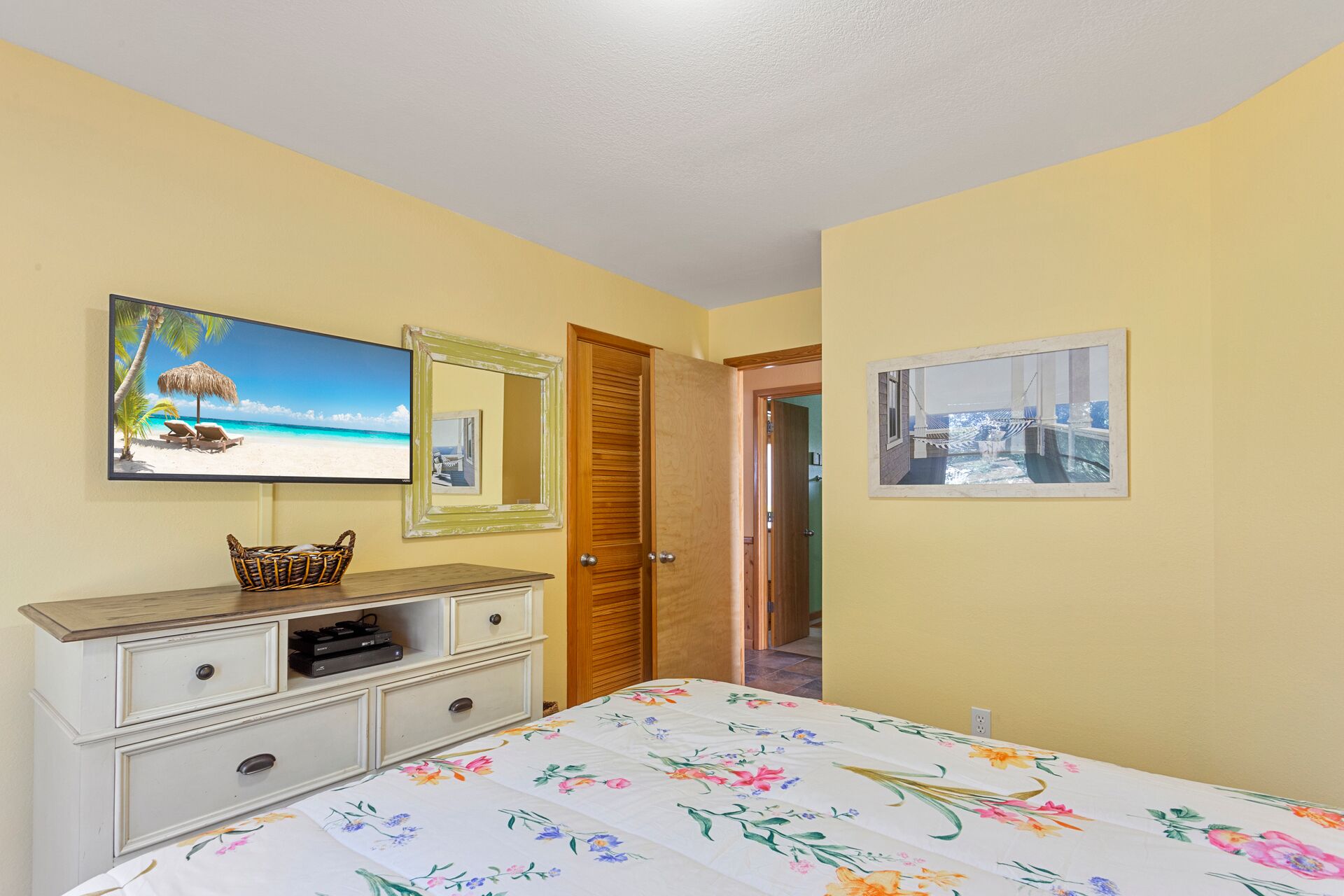 Ein Schlafzimmer mit einem Bett, einem Schminktisch, einem Fernseher und zwei gerahmten Bildern an der Wand.