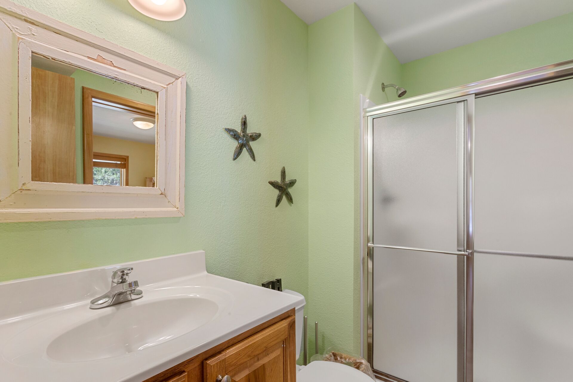 A bathroom with a white sink, wooden cabinets, a mirror, and two starfish wall decorations.