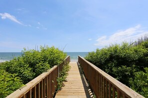 A wooden boardwalk leading to a beach with dense green foliage on either side. - Sea Spirit OBX Dog Friendly Oceanfront HotTub (Corolla)