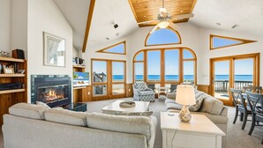A spacious living room with a fireplace, comfortable seating, and large windows offering ocean views. - Sea Spirit OBX Dog Friendly Oceanfront HotTub (Corolla)
