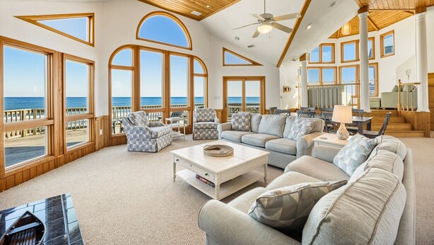 A spacious living room with large windows, a ceiling fan, and a view of the ocean. - Sea Spirit OBX Dog Friendly Oceanfront HotTub (Corolla)