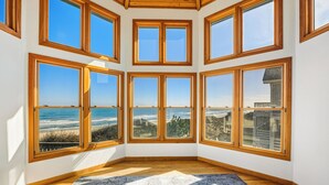 A room with multiple large windows offering ocean views, wooden flooring, and a patterned rug. - Sea Spirit OBX Dog Friendly Oceanfront HotTub (Corolla)