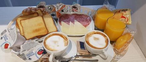 A breakfast tray with toast, cheese, salami, two cups of coffee, juice, and packaged snacks.