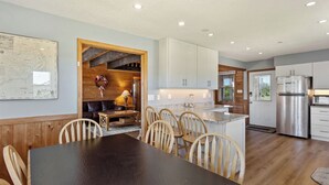 A modern kitchen with white cabinets, a stainless steel refrigerator, and a dining area with a dark table and wooden chairs.