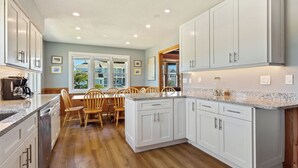 A modern kitchen with white cabinets, a granite countertop, and wooden chairs around a breakfast table.