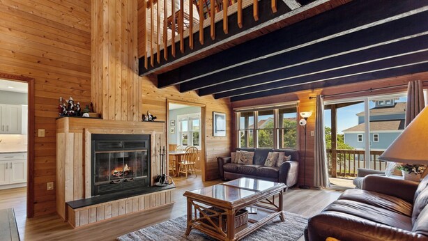 A cozy cabin interior with a fireplace, wooden floors, a leather sofa, and large windows.