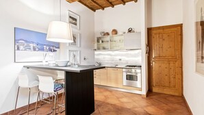 Una cucina con isola centrale, sedie bianche, soffitto in legno e una porta.