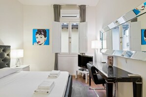 A hotel room with a bed, a desk, a chair, a television, and a large mirror.