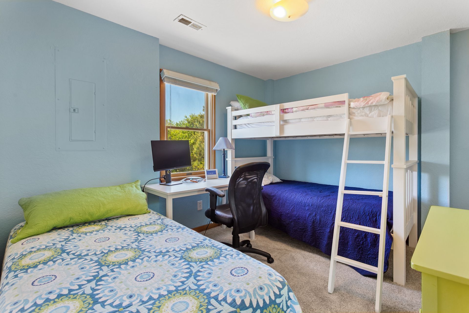 A room with bunk beds, a desk with a computer, a chair, and a bed with a patterned bedspread.