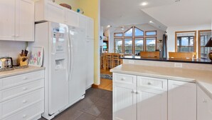 Una cocina moderna con armarios blancos, un refrigerador empotrado y un comedor con mobiliario de madera.