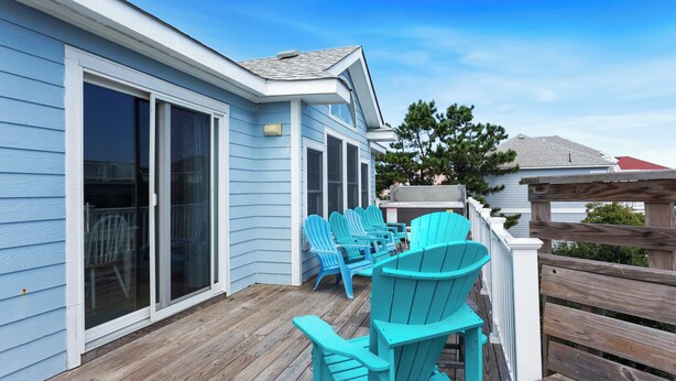 Een overdekt terras met turquoise Adirondack-stoelen, een houten tafel en een schuifdeur naar een patio.