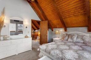 A bedroom with a large bed, a dresser, a mirror, and a ceiling with exposed wooden beams. - Eureka: 50ft to Beach, Ocean Views, Cozy Retreat (Corolla)