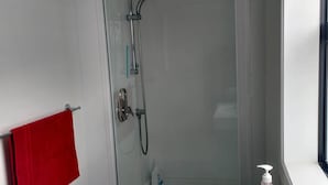 A bathroom with a glass-enclosed shower, a white sink, and a red towel hanging on a rack. - Omanu Beach Break - Walk across the road to the beach, close to golf (Mount Maunganui)