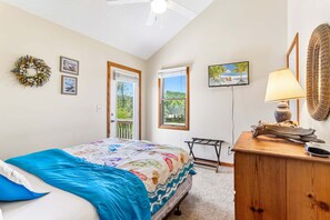 Ein Schlafzimmer mit Bett, Kommode, Fernseher, Fenster und Tür.