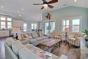 A spacious living room with a sofa, armchairs, and a coffee table. There is a dining area with a table and chairs, and a kitchen in the background. - Beach Haven: 3-Min Walk Beach, Pool, Hot Tub (Kitty Hawk)