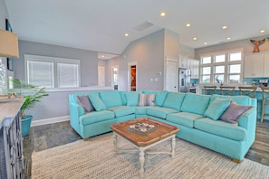 Un salon spacieux avec un canapé d’angle turquoise, une table basse en bois et une cuisine en arrière-plan.