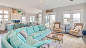 A spacious living room with a teal sofa, wicker chairs, and a coffee table. - Bikinis & Martinis: Walk Beach, Pool, Hot Tub (Kitty Hawk)