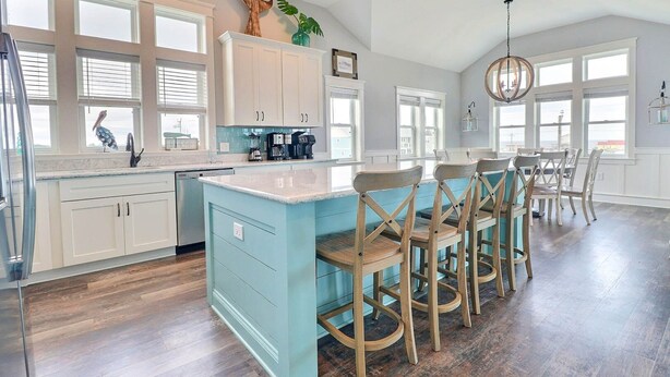 A spacious kitchen with a large island, white cabinetry, and a dining area with wooden chairs. - Bikinis & Martinis: Walk Beach, Pool, Hot Tub (Kitty Hawk)