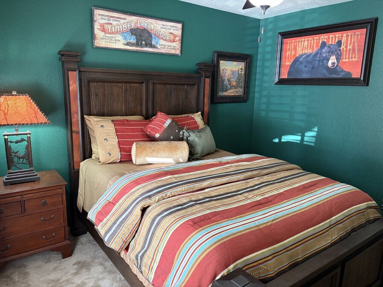 Een slaapkamer met een houten bed, gestreept beddengoed, een lamp en wanddecoratie, waaronder een waarschuwingsbord met een beer.