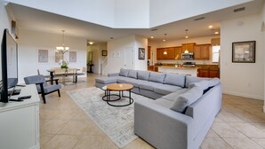 A spacious living area with a gray sectional sofa, a coffee table, and a TV on a white cabinet. A dining area with a table and chairs is visible in the background. - 5 Mi to Walt Disney World! Gem w/ Resort Perks (Kissimmee)