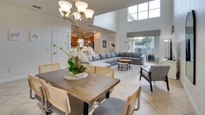 A spacious living room with a large gray sectional sofa, a dining area with a wooden table and wicker chairs, and a kitchen in the background. - 5 Mi to Walt Disney World! Gem w/ Resort Perks (Kissimmee)