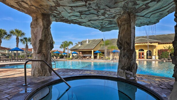 A pool area with stone pillars, a clear blue pool, and a building with a yellow facade in the background. - 5 Mi to Walt Disney World! Gem w/ Resort Perks (Kissimmee)